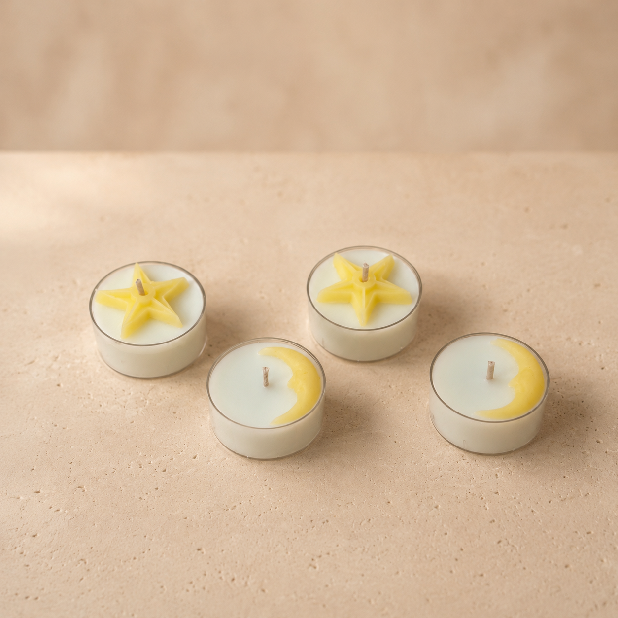 Set of four tea lights with star and crescent moon wax details on a beige stone surface